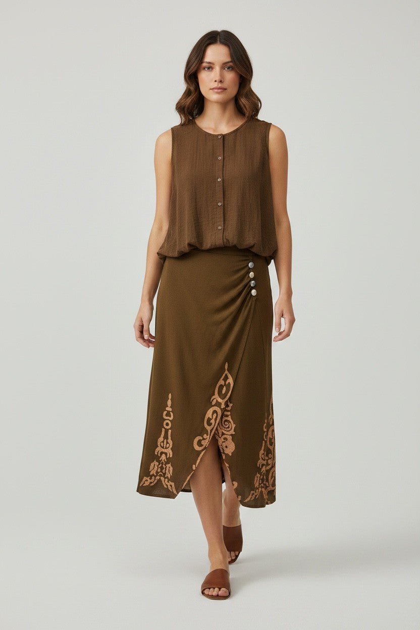 Model draagt mouwloze bruine top met knoopsluiting, gecombineerd met lange rok met decoratieve print en knopen, uit de Chastar Nieuw collectie Sets.