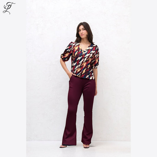 Damesmodel draagt Chastar Soft Top Mila met opvallende print en pofmouwen, gecombineerd met bordeaux broek uit zomercollectie.