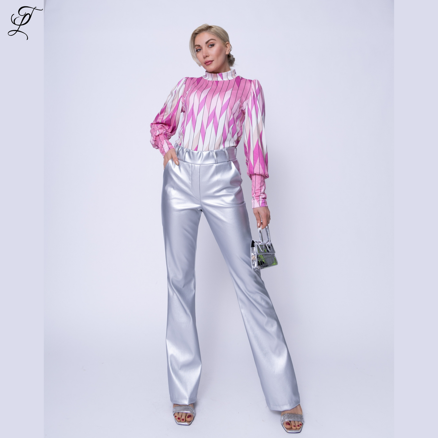 Modieuze Chastar PU Flair Broek Lila gedragen met roze-wit geometrische blouse. De broek heeft een glanzende zilveren afwerking en uitlopende pijpen. Een kleine handtas en sandalen complementeren de look. Home page, Broeken, Collectie.
