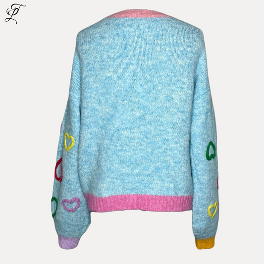 Chastar Hart Sweater in lichtblauw met kleurrijke hartjes decoraties en contrasterende roze, paarse en gele boorden. Oversized trui met comfortabele pasvorm getoond vanaf de achterkant. Truien, Collectie, Bestsellers.