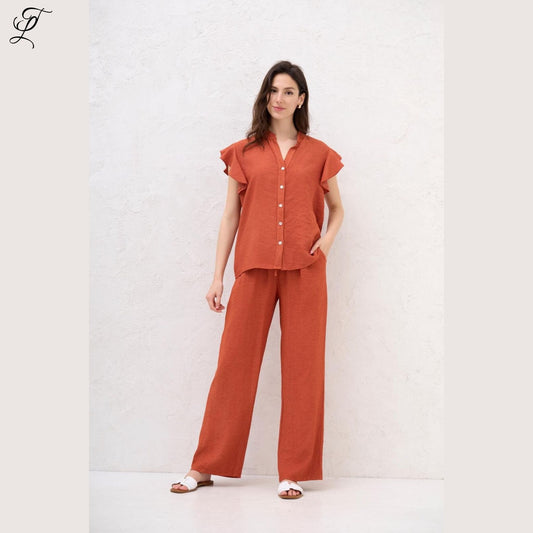 Vrouw draagt de Chastar Linnen Blouse in roest met ruffle-mouwen en knoopsluiting, perfect voor zomerse dagen.