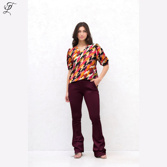Vrouw draagt Chastar Soft Top Mila met opvallende print, pofmouwen en comfortabele pasvorm in bordeaux en oranje tinten.
