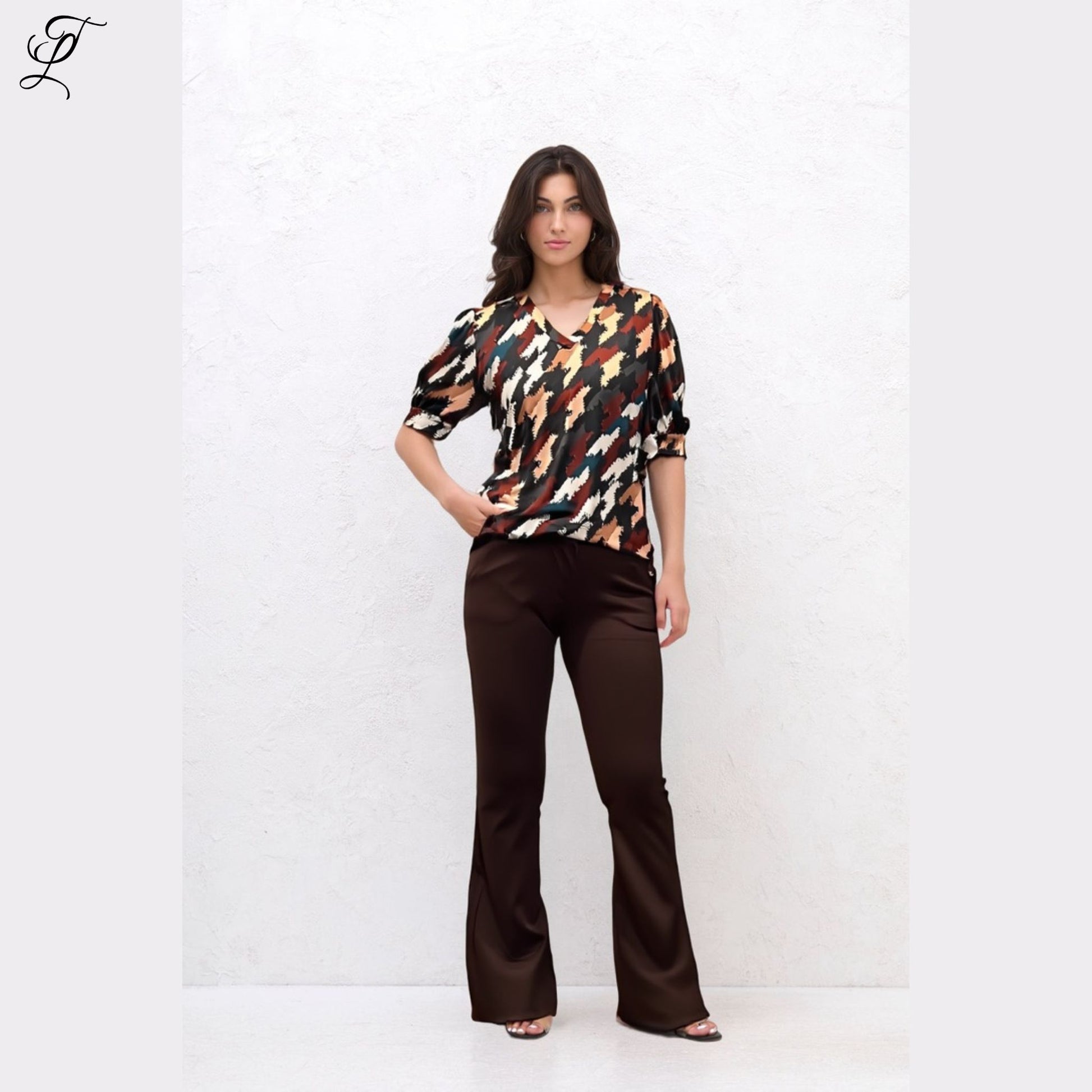 Vrouw draagt Chastar Soft Top Mila met opvallende print en pofmouwen, gecombineerd met elegante bruine broek.