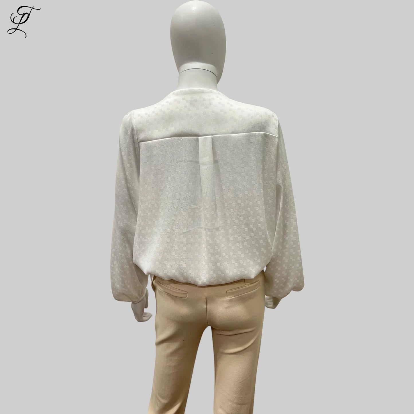 Chastar V-Hals Blouse getoond op een paspop, achterzijde weergave met subtiel ingeweven patroon in off-white. Elegante loose-fit stijl met lange mouwen en elastische manchetten, gecombineerd met een beige broek. Blouses, Collectie