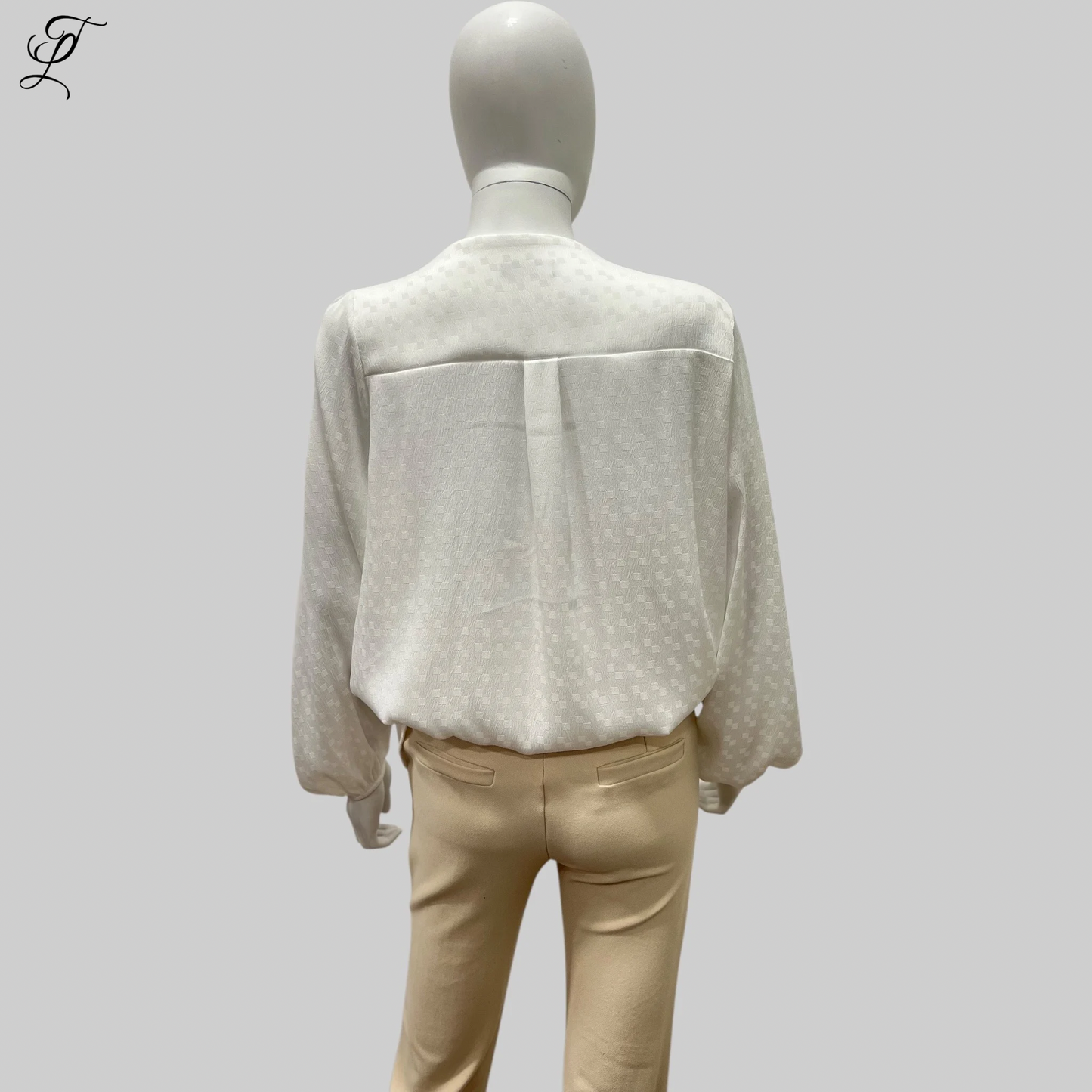 Chastar V-Hals Blouse getoond op een paspop, achterzijde weergave met subtiel ingeweven patroon in off-white. Elegante loose-fit stijl met lange mouwen en elastische manchetten, gecombineerd met een beige broek. Blouses, Collectie