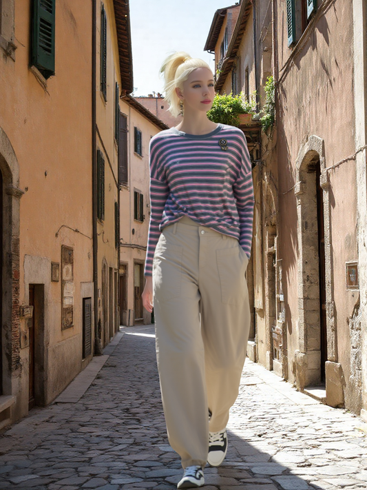 Vrouw draagt oversized lange mouw T-shirt in roze en grijs met beige broek op een zonnige straat in Italië.