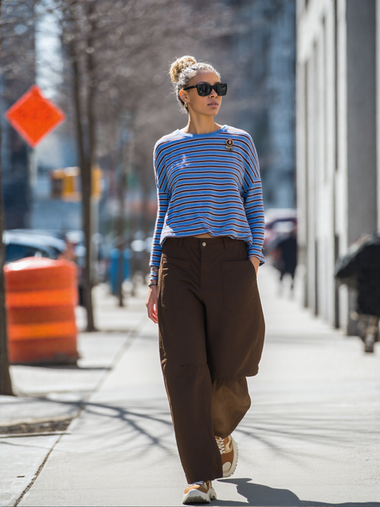 Vrouw draagt oversized lange mouw t-shirt met blauwe en bruine strepen gecombineerd met wijde bruine broek en zonnebril.