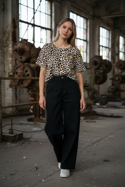 vrouw met beige panterprint shirt en zwarte wijde broek in industrieel gebouw met grote ramen
