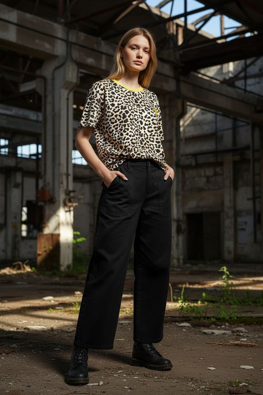 Vrouw draagt luipaardprint shirt met gele halslijn en zwarte wijde broek in industrieel, licht beschaduwd magazijn.