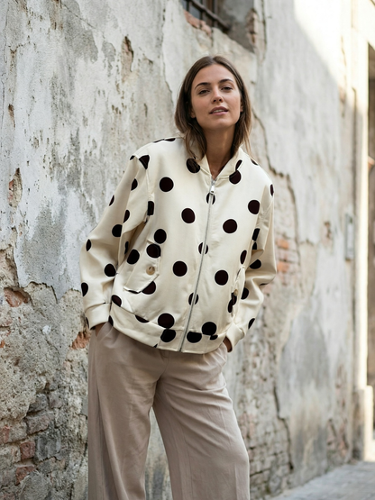 vrouw met beige jack met grote zwarte stippen tegen verweerde muur in steegje