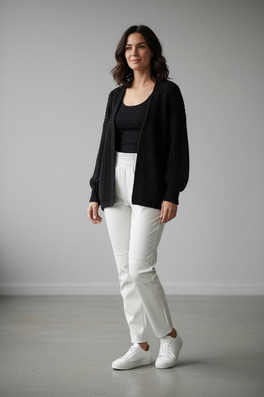 Vrouw draagt zwarte gebreide vest uit de Herfst Collectie met witte broek en witte sneakers van Chastar.