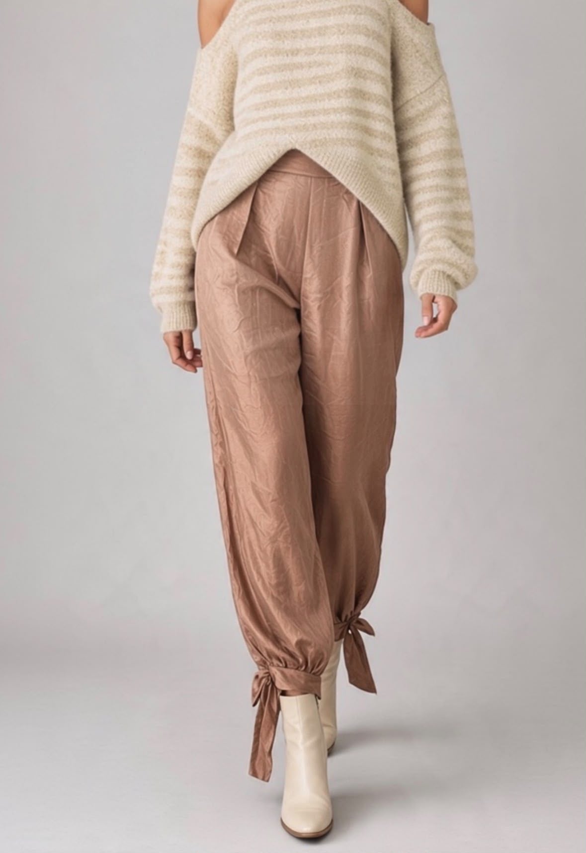 Bruine Chastar broek met plooien en strikdetails aan de enkels, gedragen met een gestreepte trui.