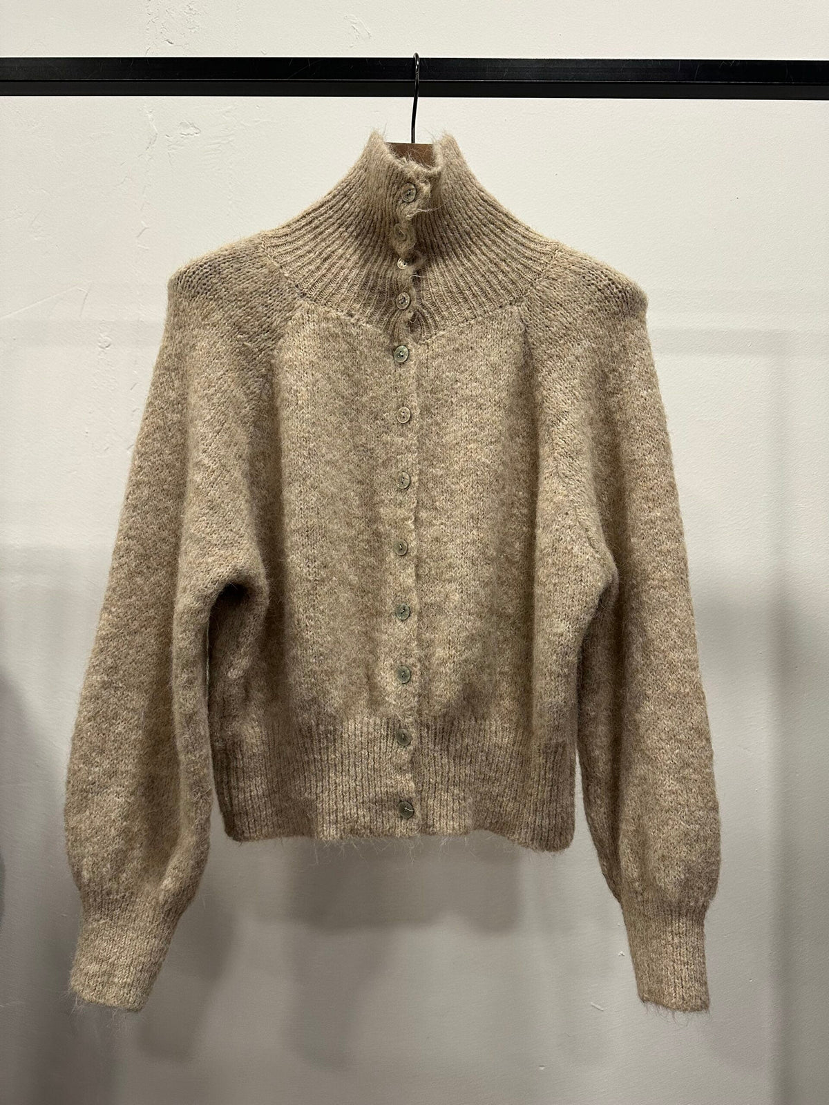 Chastar Cardigan Gebreid met hoge kraag in beige met knoopsluiting en geribde boorden, aan een kledinghanger.