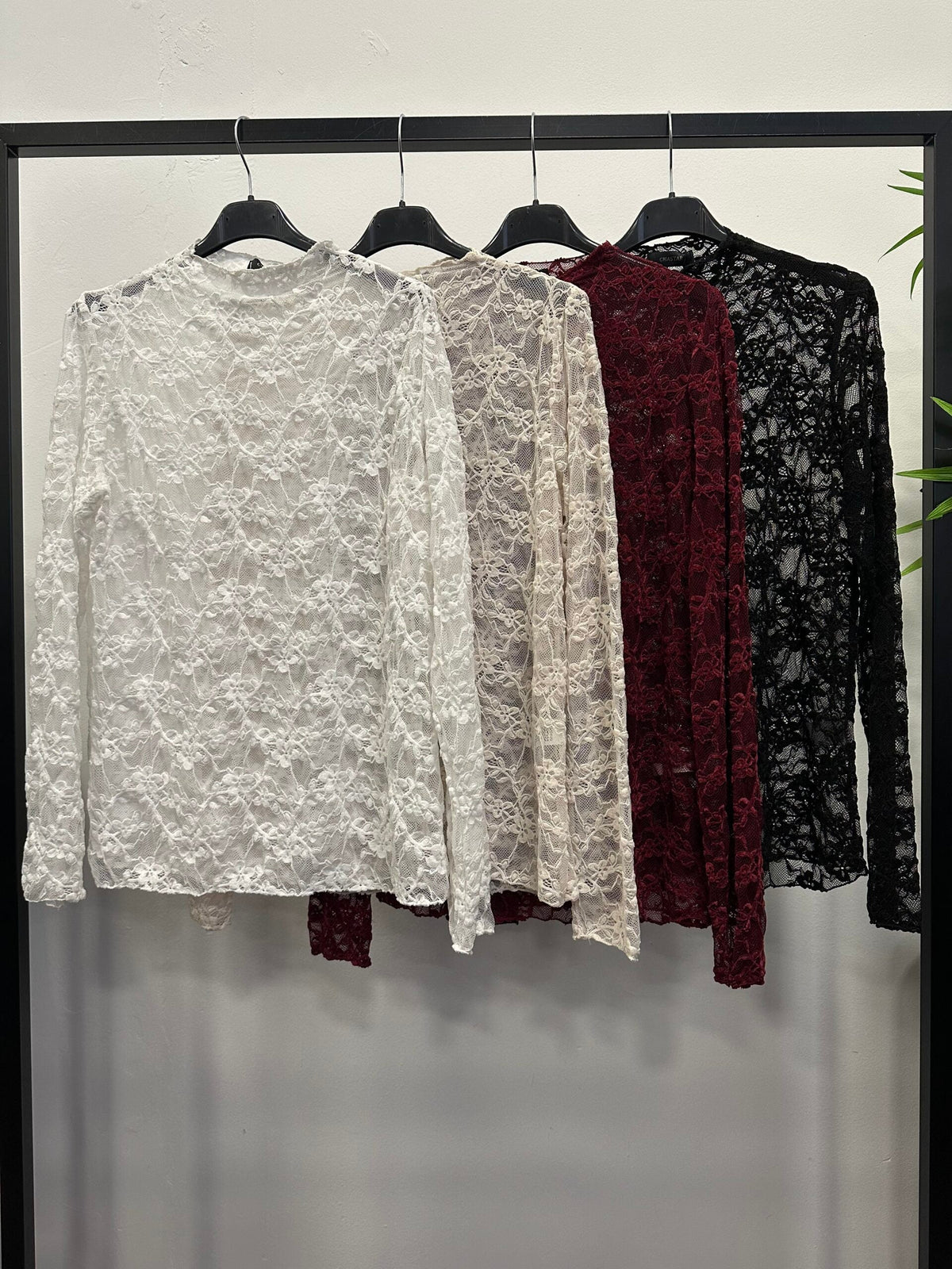Chastar Top Elora met transparant bloemmotief en hoge hals in wit, off white, bordeaux en zwart aan een kledingrek.