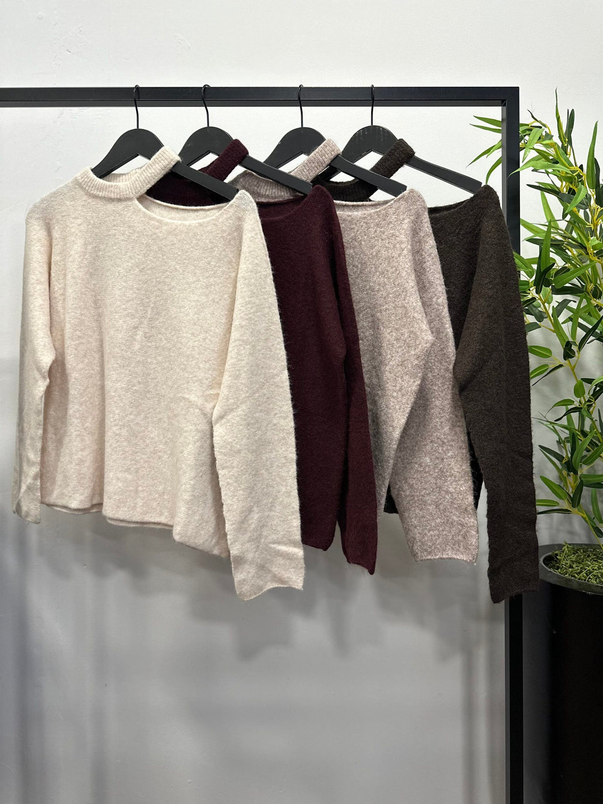 Chastar Trui met schouderdetail in vier kleuren aan een kledingrek, met ronde hals en uitsparing bij de schouder.